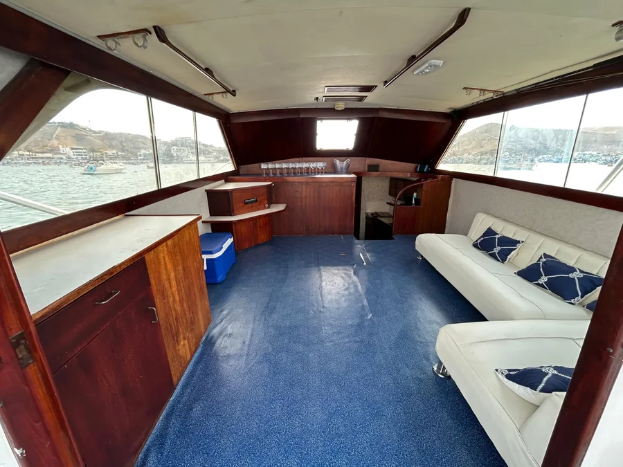 Salón interior del yate, con sofá corrido, barra y vista a la bahía de Pucusana